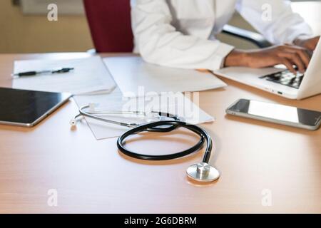 Crop African American female doctor typing report on laptop while working at table in modern clinic office Stock Photo