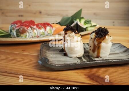 Gunkan sushi and Uramaki rolls served on plates on wooden table in Japanese restaurant Stock Photo