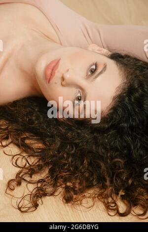 From above of tender female in beige bodysuit lying on wooden floor and looking at camera Stock Photo