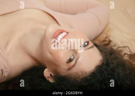 From above of tender female in beige bodysuit lying on wooden floor and looking at camera Stock Photo