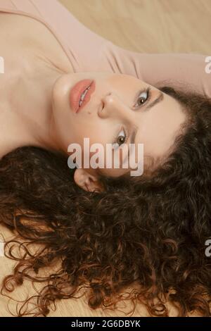 From above of tender female in beige bodysuit lying on wooden floor and looking at camera Stock Photo