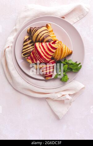 Top view of delicious croissants placed on plate with sprig of mint on pastel pink background Stock Photo