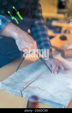 Crop unrecognizable male woodworker using professional compass or divider while marking wooden plank at workbench in carpentry workshop Stock Photo