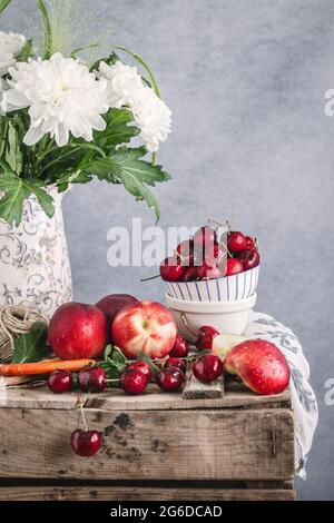 Still life of ripe nectarines and cherries placed on rustic table with flowers in vase on gray background in studio Stock Photo