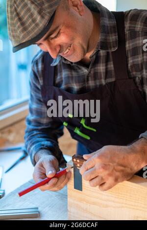 Positive professional woodworker with pencil and measuring tool making marks on timber board while creating handicraft object in carpentry workshop Stock Photo