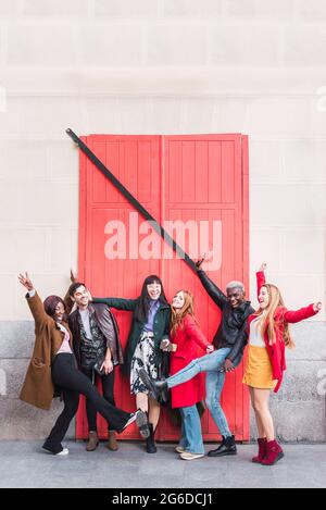 Group of excited multiracial friends having fun in city while standing on street with raised arms Stock Photo