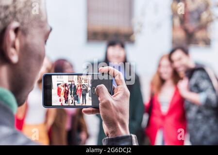 Back view of unrecognizable black male taking photo of company of multiracial friends standing on street together Stock Photo