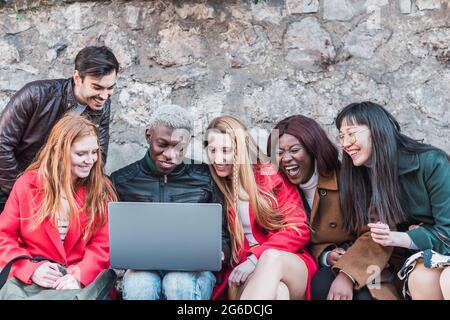 Company of diverse students doing homework together while using netbook in city street Stock Photo