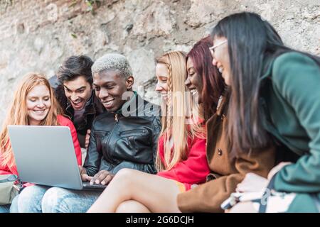 Company of diverse students doing homework together while using netbook in city street Stock Photo