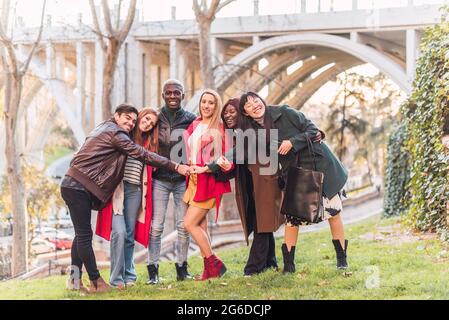 Company of happy diverse friends hugging while standing on lawn in park and looking at camera Stock Photo