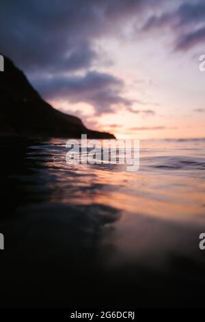 Waving blue sea rolling over seashore near distant mountain during sunset Stock Photo