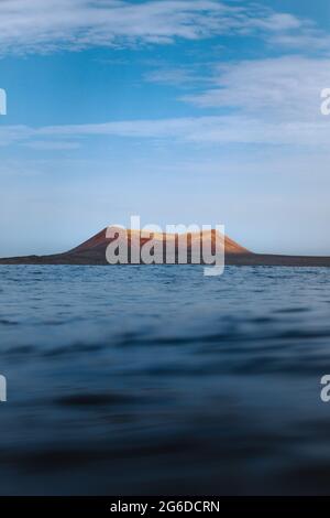 Waving blue sea rolling over seashore near distant mountain Stock Photo