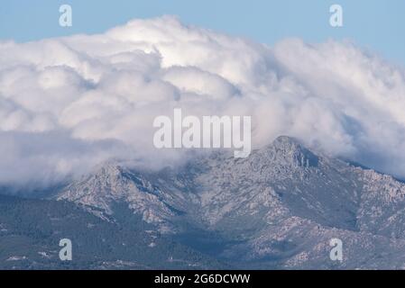 Thick white clouds covering top of breathtaking mountain range against blue sky in Sierra de Guadarrama National Park in Madrid, Spain Stock Photo