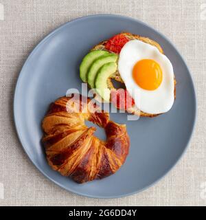 Plate viewed from above with croissant and an avocado egg toast Stock Photo