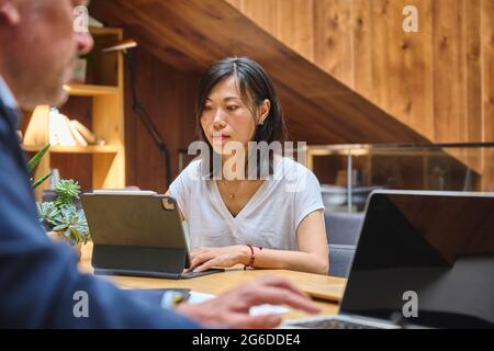 Asian girl working in her laptop at the office with other coworker Stock Photo
