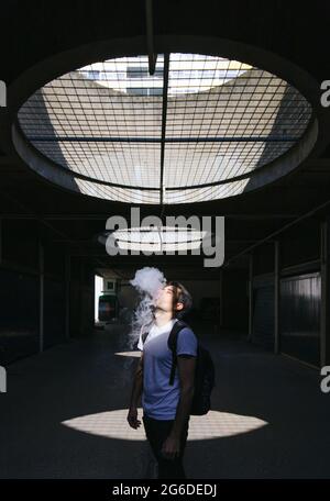 man exhaling vapour standing in underground alley passage with round windows in ceiling with sunlight shining Stock Photo