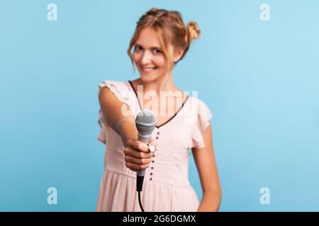 Young adult beautiful woman reporter in summer dress holding microphone, making interview and asking opinion, discussing important topics. Indoor stud Stock Photo