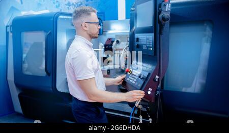 Worker man entering data in CNC machine at automatic factory floor. Modern process metal detail production going for car. Stock Photo