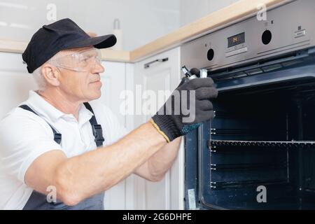 Service for repair, plumber man in uniform repairing oven heat machine. Stock Photo