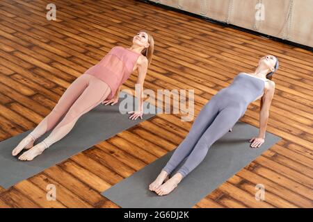 Two women in sportswear practicing yoga asana Purvottanasana doing the reverse plank Stock Photo