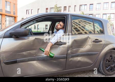 Stop drink alcohol. Do not drive drunk. Man driving automobile after drinking beer, falling asleep after collisions and vehicle damage, holding bottle Stock Photo