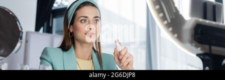 young woman holding spray bottle of micellar water near ring lamp, banner Stock Photo