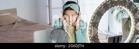 stylish beauty blogger adjusting headband while preparing to video record near phone holder, banner Stock Photo