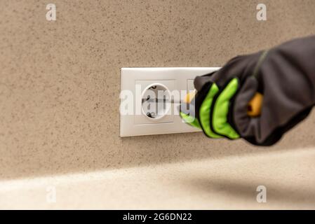 The electrician installs a decorative frame on the electrical outlets. Screwdriver in the hands of a master installing a socket with gloves. Stock Photo