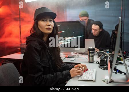 Serious female hacker sitting in front of computer against two guys Stock Photo