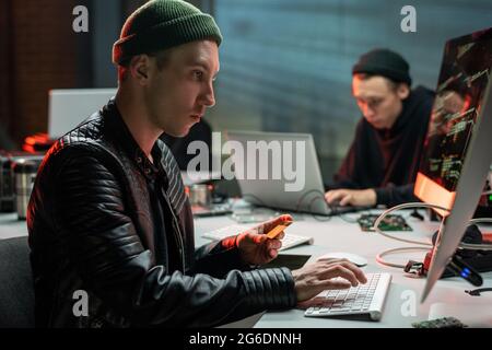 Criminal with plastic card looking at computer screen in office Stock Photo
