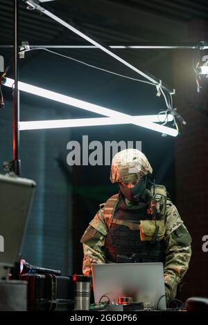Hacker in camouflage attire using laptop while stealing information from database Stock Photo