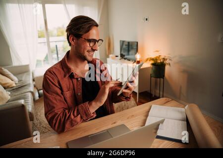Caucasian male student working from home typing on digital tablet wearing spectacles Stock Photo