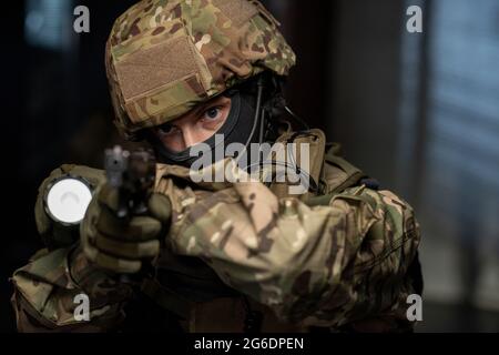 Young man in camouflage protective attire and mask using lantern and gun Stock Photo