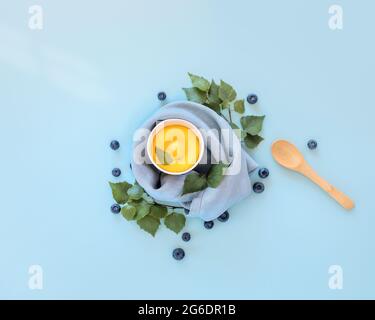 Summer, eco friendly, food composition with yellow, homemade, fruit ice cream, blueberries and a wooden spoon on a blue background. Vegan ice cream Stock Photo