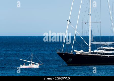 Stunning view of an old, wooden boat with tourists on board sailing in front of a luxury yacht. Costa Smeralda, Sardinia, Italy. Stock Photo