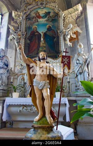 Jesus Resurrection statue with the maltese cross flag inside the church in front of altar with painting of Saint Peter and Paul. Stock Photo