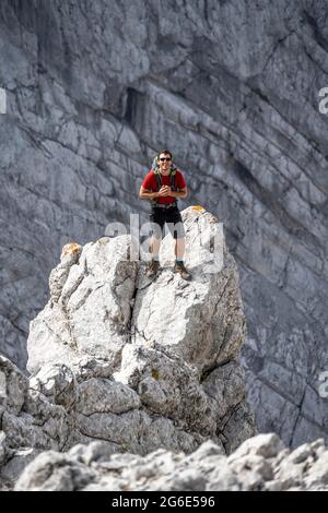 Young man standing on rocks, Rocky mountains and scree, Hiking to the Hochkalter, Berchtesgadener Alpen, Berchtesgadener Land, Upper Bavaria Stock Photo