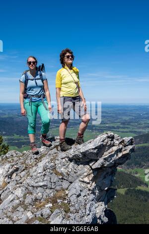 Two female hikers looking over the alpine foothills, on the summit of Breitenstein, Fischbachau, Bavaria, Germany Stock Photo