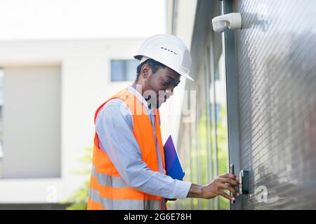 Young black man works outside as technician checks with smartphone and helmet and safety vest, Freiburg, Baden-Wuerttemberg, Germany Stock Photo