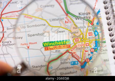 Closeup of a page in a printed road map atlas with a man's hand holding a magnifying glass showing an enlargement of the city of Winchester in England Stock Photo