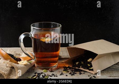 A glass mug of fragrant brewed flower tea on a wooden table, with tea leaves in a paper package, in a rustic style. Selective focus. Stock Photo