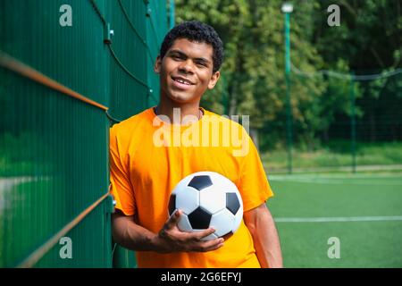 African-American man holding soccer ball while standing against fence Stock Photo