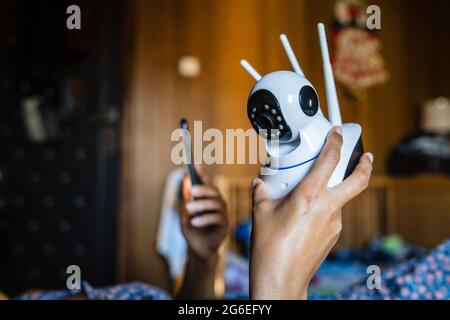 Close up on midsection of unknown woman holding home security surveillance camera and mobile phone trying to install an app while lying on bed side vi Stock Photo