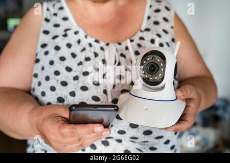 Close up on midsection of unknown woman holding home security surveillance camera and mobile phone trying to install an app front view copy space Stock Photo