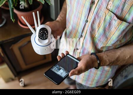 Close up on midsection of unknown man holding home security surveillance camera and mobile phone trying to install an app top view copy space Stock Photo