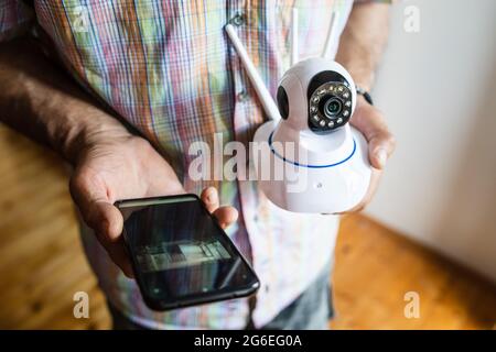 Close up on midsection of unknown man holding home security surveillance camera and mobile phone trying to install an app top view copy space Stock Photo