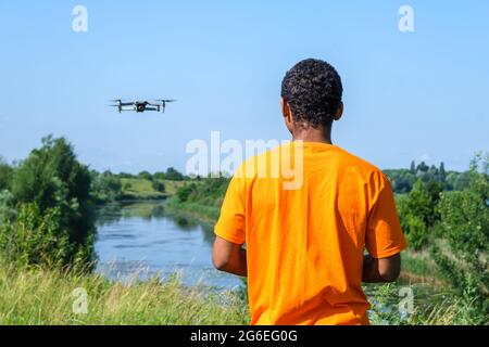 African American man operating drone with controller on the meadow with back Stock Photo