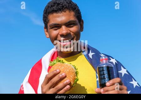 African American man with flag enjoying hamburger and cola drink outdoor Stock Photo