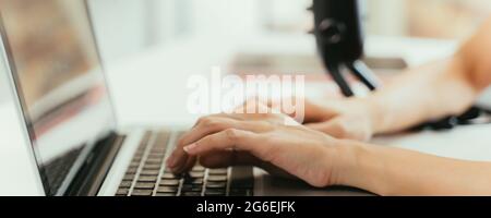 Closeup of young beautiful woman smiling sitting on desk using laptop and mic recording podcast while taking interview Stock Photo