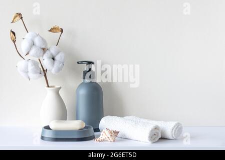 Bathroom interior in beige pastel tone. White shelf in bathroom with towels, soap, shampoo bottle, houseplant. Mockup with space for text. Minimal com Stock Photo